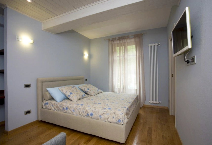 foto principale della camera Iris con un letto matrimoniale, una televisione a muro e una portafinestra